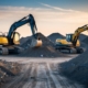 A construction site with a tracked and wheeled excavator side by side, surrounded by piles of dirt and rocks. The excavators are in the process of digging and moving materials